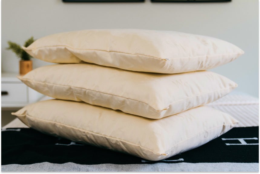 Three wool pillows stacked on a bed showing different loft sizes